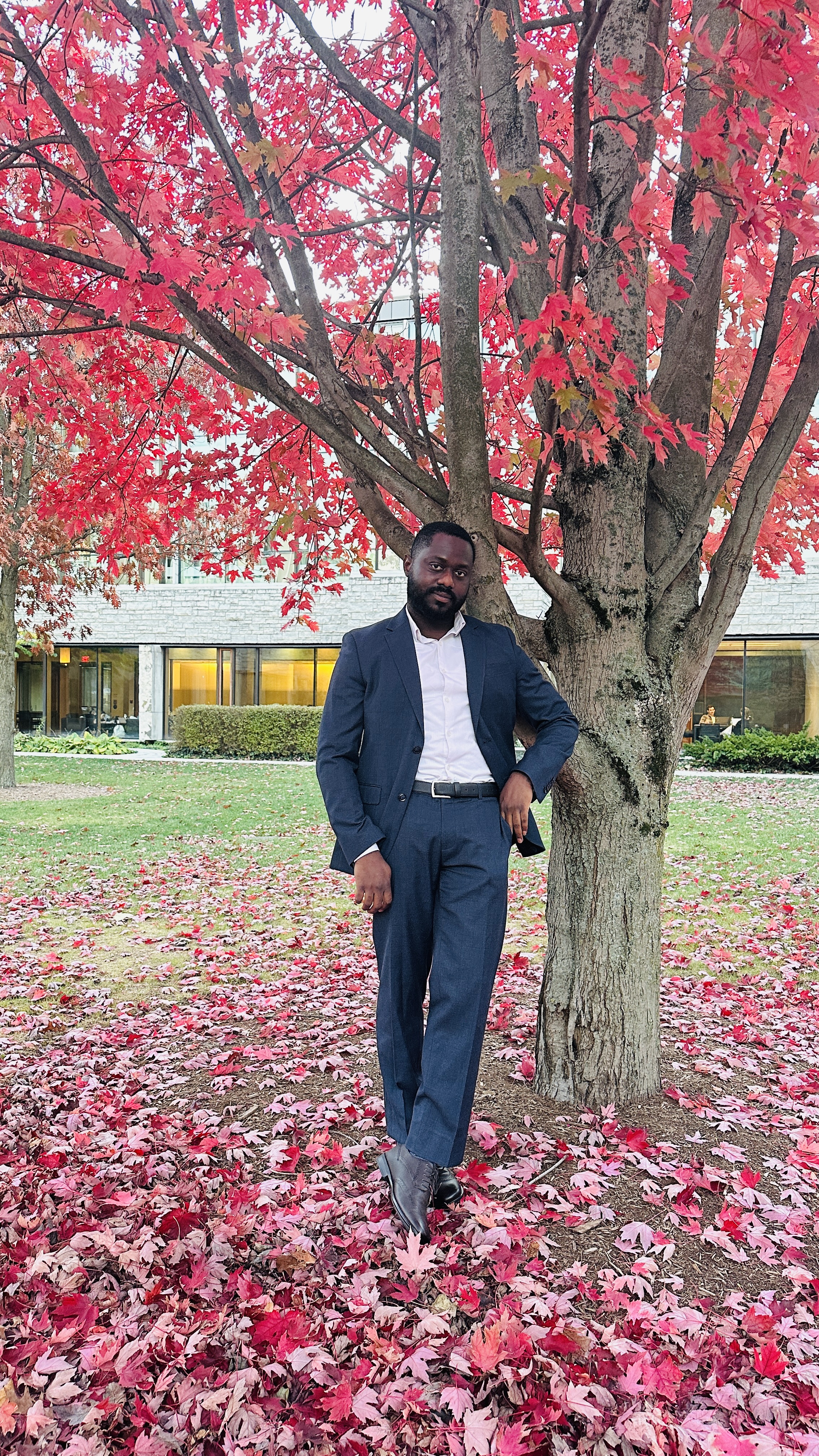 Daniel Ebitunmise standing beside a red-leafed tree
